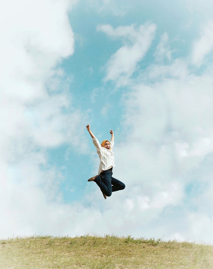 services-07 A person jumping energetically on a grassy hill under a bright blue sky with scattered clouds.
